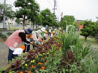 会員とオレンジ帽子の子供たちが並んで花壇の手入れ