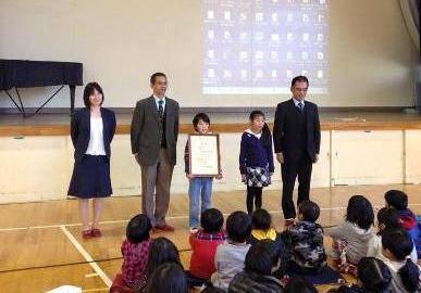 写真：受賞者（表彰状を持つ松田さんと佳作の松岡さん）審査委員で記念撮影
